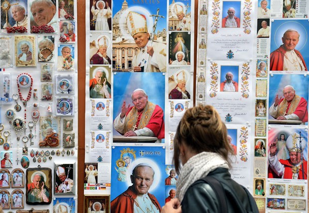 Mulher passa por pôsteres e cartões postais com a imagem do Papa João Paulo II em Roma (Foto: Stefano Rellandini/Reuters)